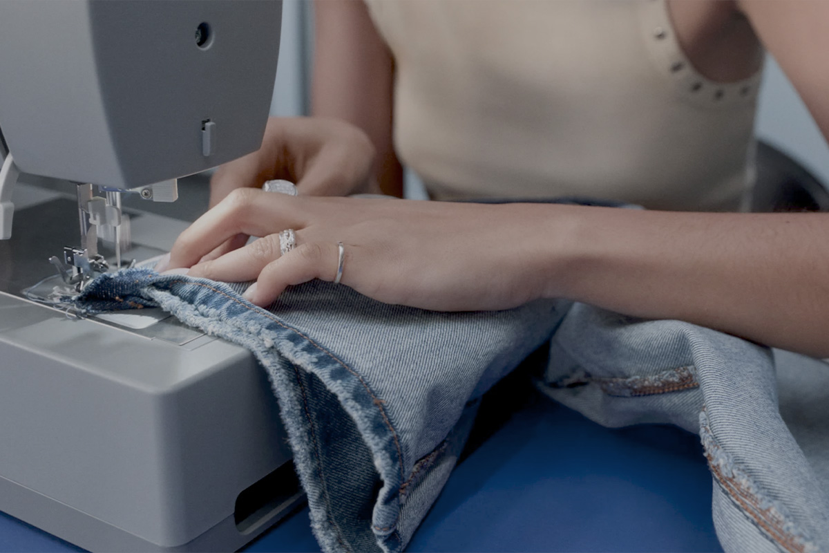 A close-up of Alima Darouiche’s hands guiding denim fabric through a sewing machine.
