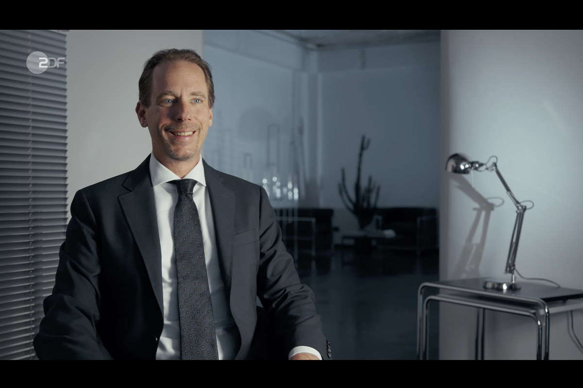 zero one film systemfehler der cum ex skandal alexander heist Interview shot of Alexander Heist in a suit, seated in a modern studio setting with minimalist decor and soft daylight, filmed for the Cum-Ex scandal documentary.