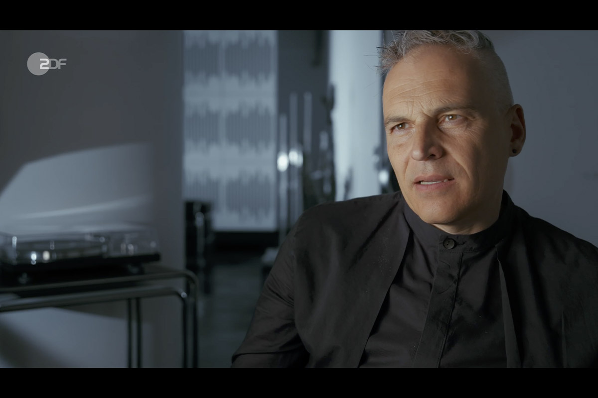 zero one film systemfehler der cum ex skandal gerhard schick Interview shot of Gerhard Schick, seated in a modern studio environment, appearing thoughtful during filming for the Cum-Ex documentary.