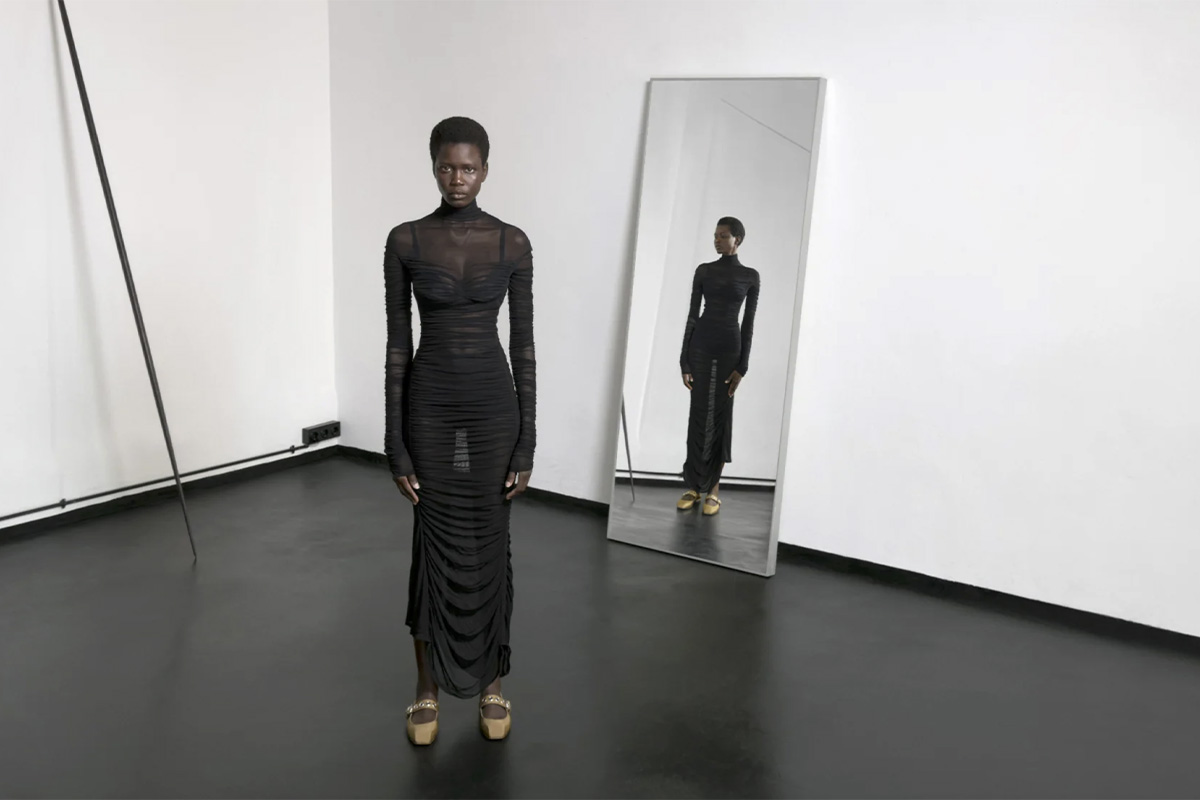 Ajah Angau standing in front of a tall mirror in a sheer black dress and gold shoes, reflecting herself inside Studio 2 at raw studios during the Sleeping Beauty shoot.