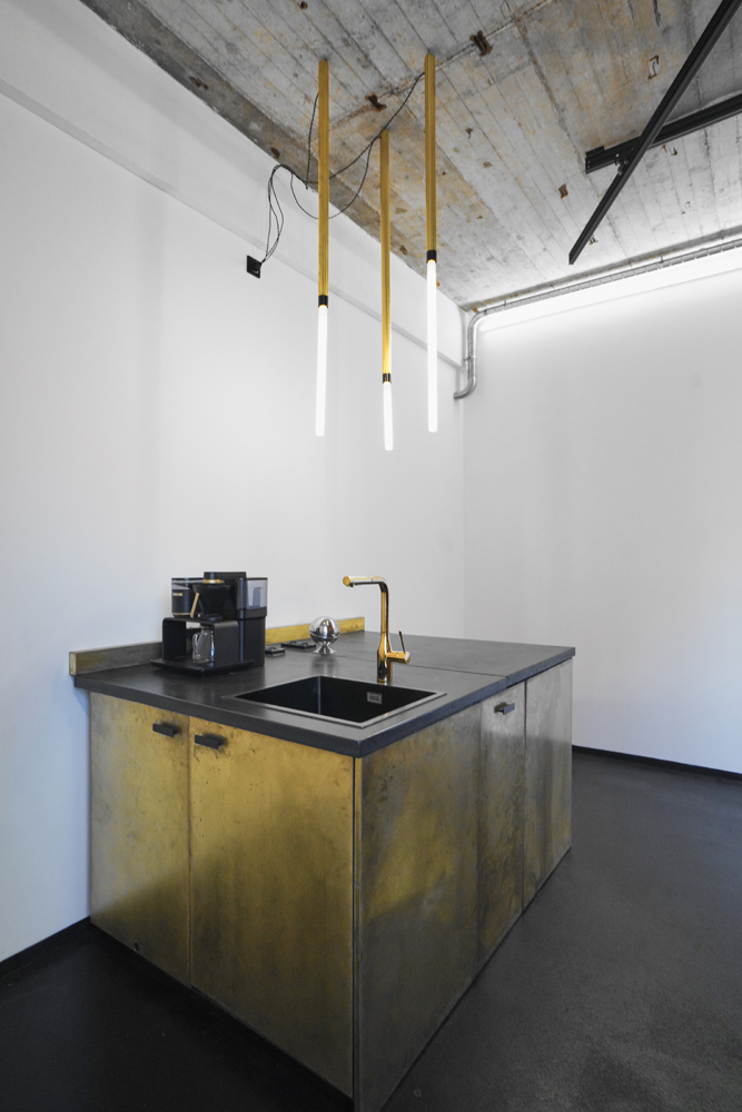 raw_studios_studio3_kitchen1_DE Kitchenette mit Designer-Holzfronten, schwarzer Arbeitsfläche und goldenen Armature