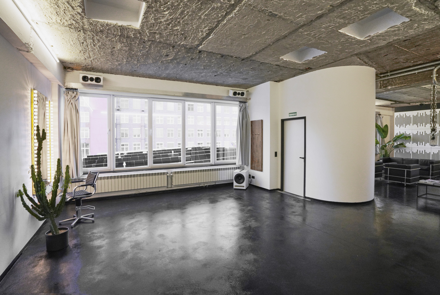 raw_studios_studio3_shootingarea1_DE Weitwinkelansicht von Studio 3, einem Tageslicht-Mietstudio in Berlin mit großen Fenstern, schwarzem Betonboden und industrieller Decke – ideal für kreative Produktionen