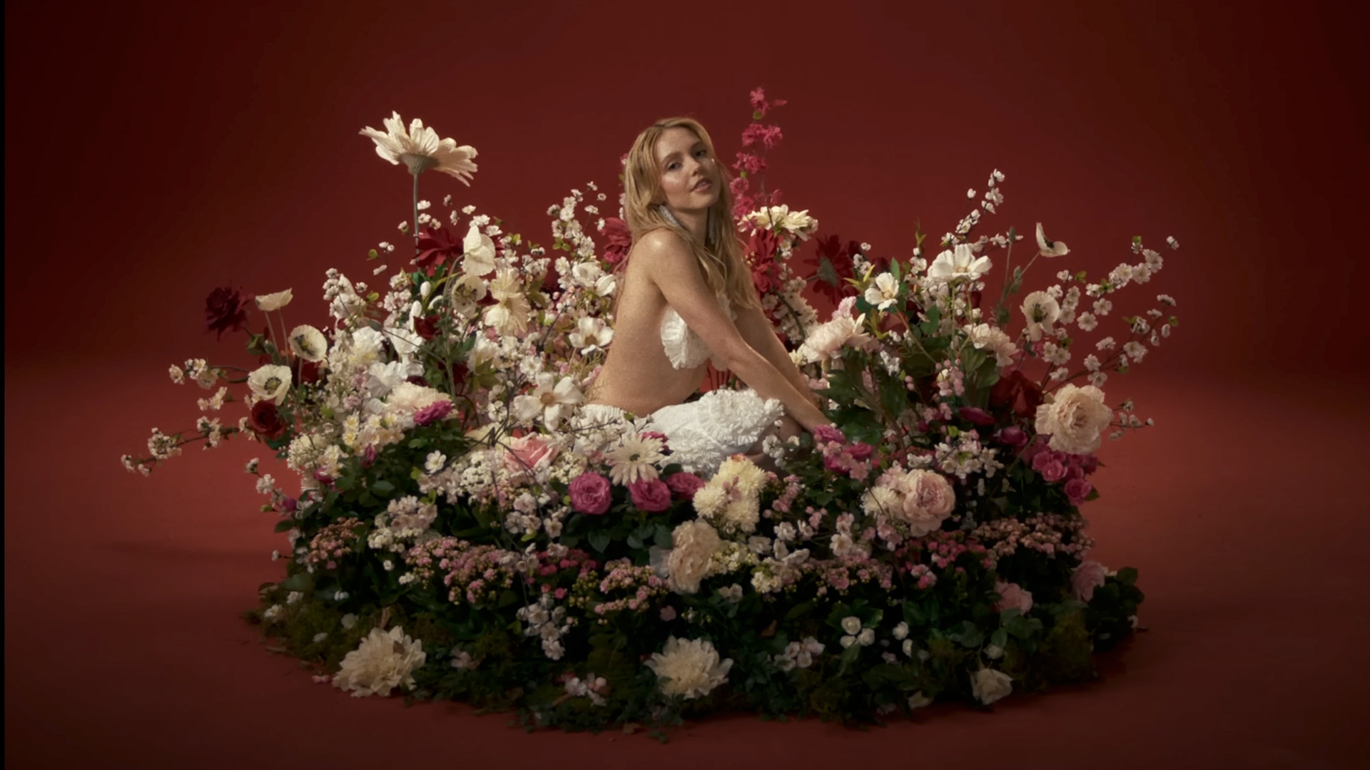 LINA surrounded by lush floral arrangement on red cyclorama, music video shoot at raw studios – foto studios berlin, rental studios berlin
